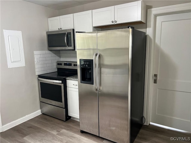 kitchen featuring electric panel, appliances with stainless steel finishes, decorative backsplash, white cabinets, and hardwood / wood-style flooring