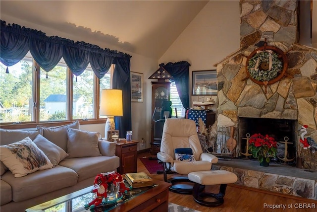 living room with hardwood / wood-style floors, a stone fireplace, and lofted ceiling