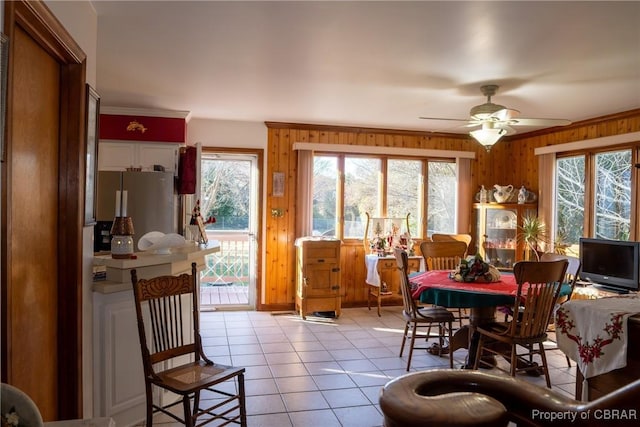 tiled dining room featuring ceiling fan, wood walls, and ornamental molding