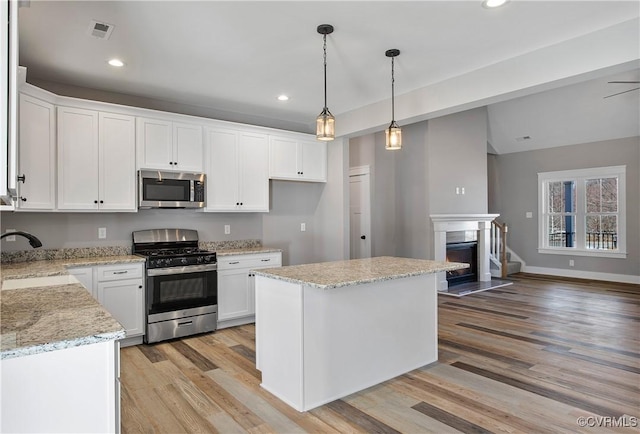 kitchen with pendant lighting, a kitchen island, sink, stainless steel appliances, and white cabinets