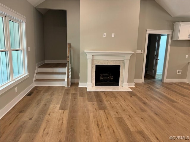 unfurnished living room with light hardwood / wood-style floors, a high end fireplace, and vaulted ceiling