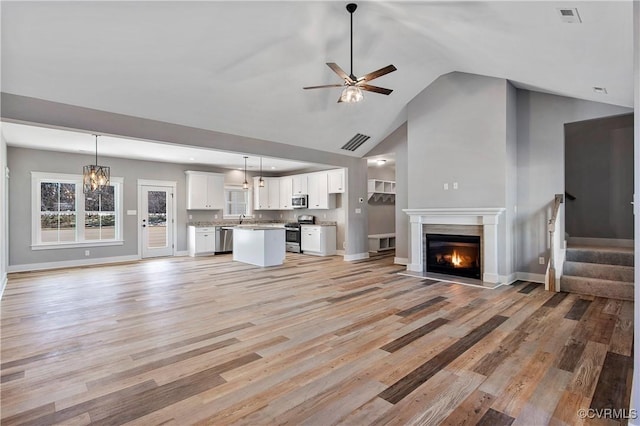 unfurnished living room with lofted ceiling, sink, ceiling fan with notable chandelier, and light hardwood / wood-style floors