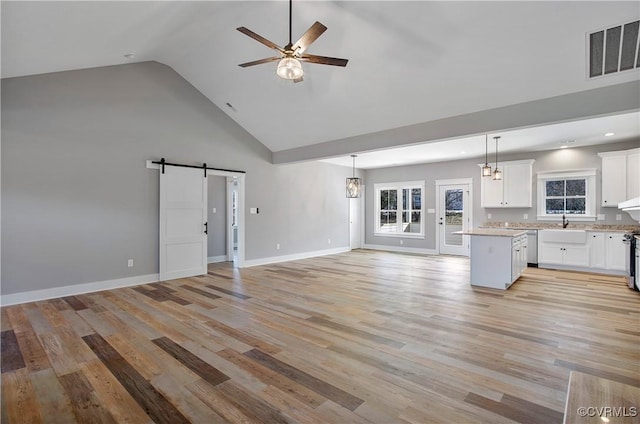 unfurnished living room featuring a barn door, high vaulted ceiling, ceiling fan with notable chandelier, light hardwood / wood-style flooring, and sink