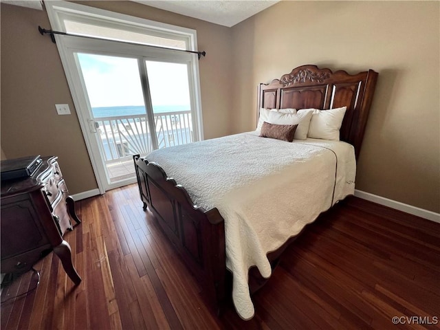 bedroom with dark hardwood / wood-style flooring, access to exterior, and a water view