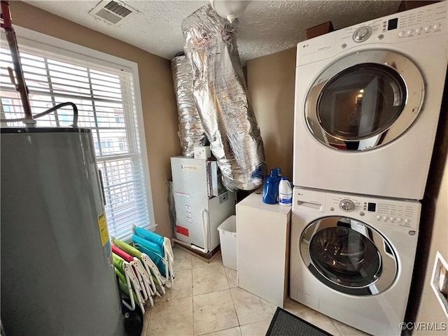 washroom with light tile patterned flooring, gas water heater, stacked washing maching and dryer, and a textured ceiling