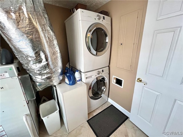 laundry area featuring a textured ceiling, light tile patterned flooring, and stacked washer and clothes dryer