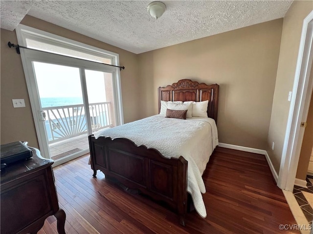 bedroom with a textured ceiling, access to outside, dark wood-type flooring, and a water view