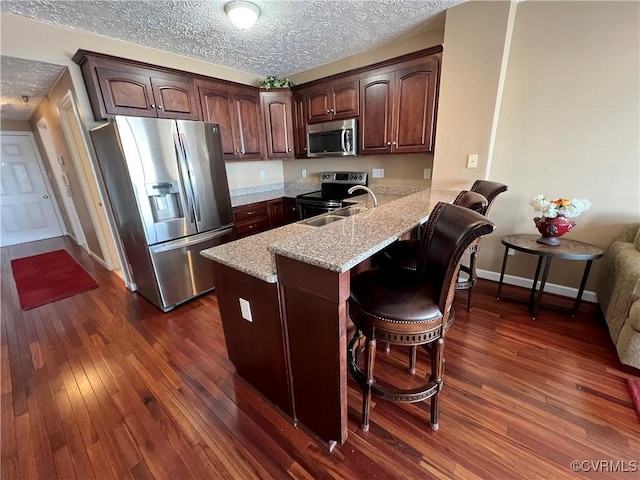 kitchen featuring kitchen peninsula, a textured ceiling, stainless steel appliances, dark hardwood / wood-style floors, and a breakfast bar area