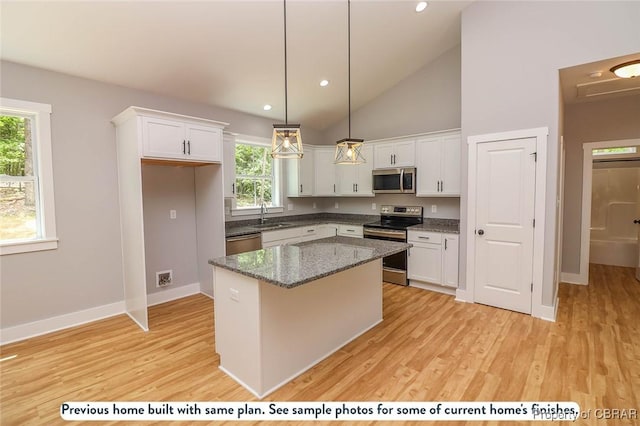 kitchen with white cabinets, appliances with stainless steel finishes, decorative light fixtures, and a kitchen island