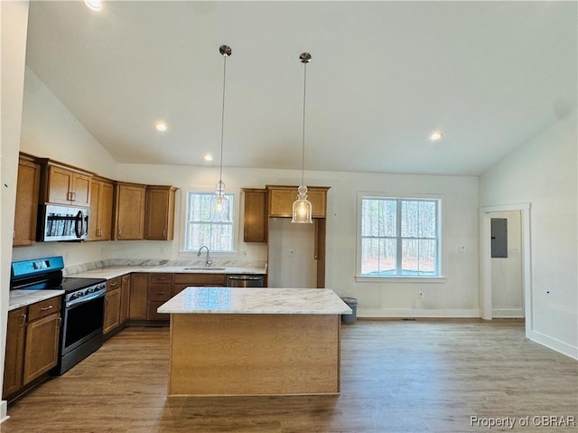 kitchen with a sink, a kitchen island, wood finished floors, appliances with stainless steel finishes, and lofted ceiling