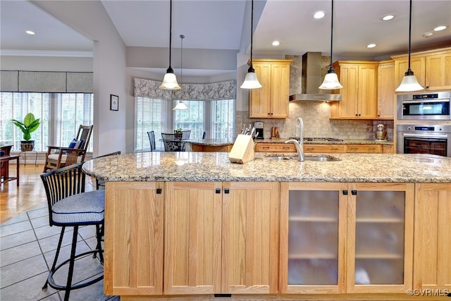 kitchen with wall chimney exhaust hood, hanging light fixtures, stainless steel appliances, decorative backsplash, and light brown cabinetry