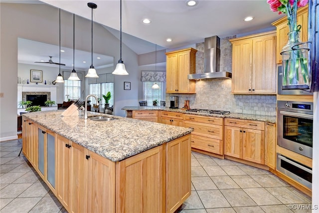 kitchen featuring wall chimney range hood, sink, light brown cabinetry, decorative light fixtures, and stainless steel appliances