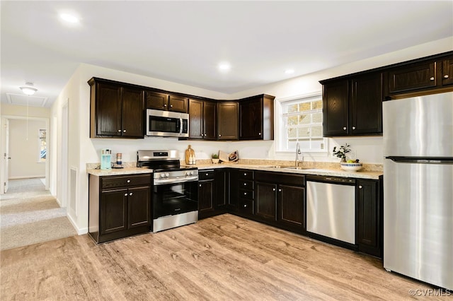 kitchen with light stone countertops, dark brown cabinetry, stainless steel appliances, sink, and light hardwood / wood-style floors