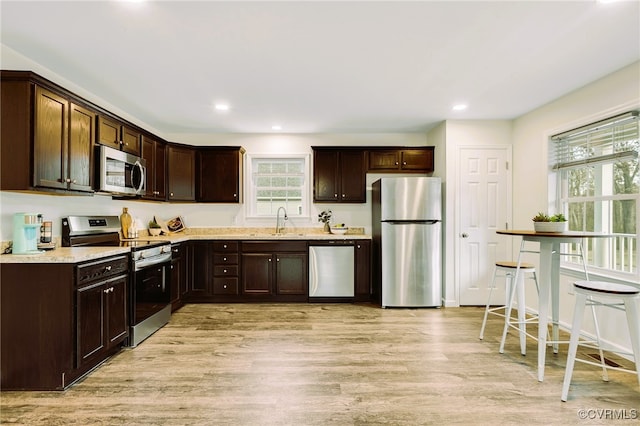 kitchen with sink, light hardwood / wood-style flooring, appliances with stainless steel finishes, light stone counters, and dark brown cabinetry