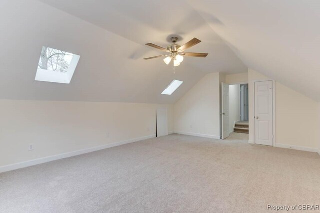 additional living space with ceiling fan, light colored carpet, and vaulted ceiling with skylight