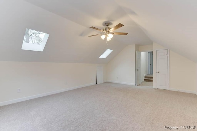 additional living space with ceiling fan, light colored carpet, and vaulted ceiling with skylight