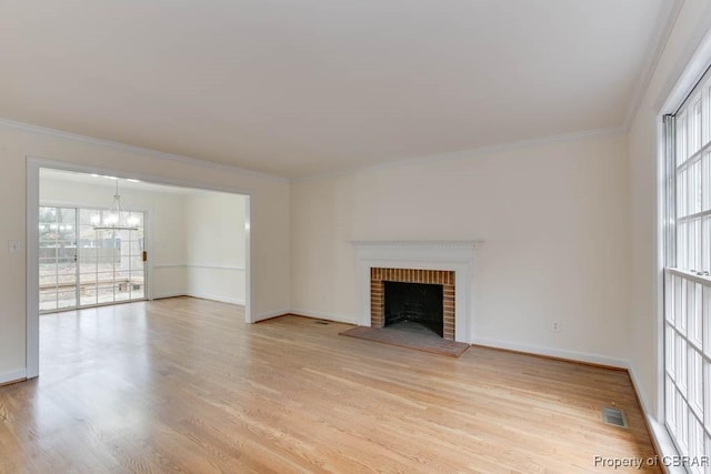 unfurnished living room featuring a notable chandelier, a brick fireplace, crown molding, and light hardwood / wood-style floors