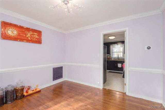 spare room featuring hardwood / wood-style floors, an inviting chandelier, and crown molding