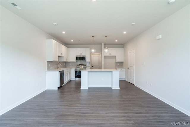 kitchen with appliances with stainless steel finishes, dark hardwood / wood-style flooring, sink, white cabinets, and a kitchen island