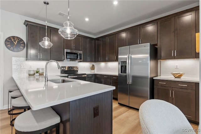 kitchen with appliances with stainless steel finishes, sink, decorative light fixtures, light hardwood / wood-style floors, and a breakfast bar area