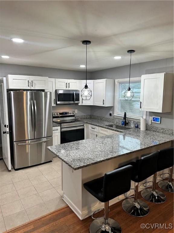 kitchen featuring kitchen peninsula, decorative light fixtures, stainless steel appliances, and stone counters