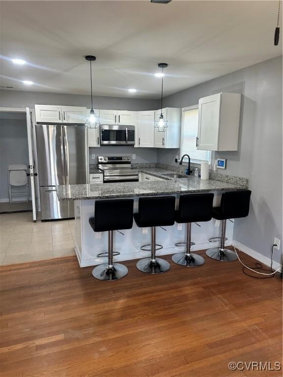 kitchen featuring kitchen peninsula, white cabinets, stainless steel appliances, and decorative light fixtures