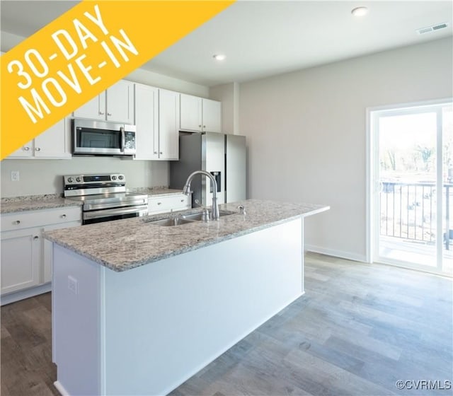 kitchen with white cabinets, appliances with stainless steel finishes, hardwood / wood-style flooring, and an island with sink