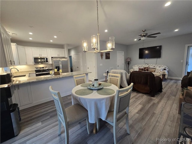 dining space with ceiling fan with notable chandelier, dark wood-type flooring, and sink