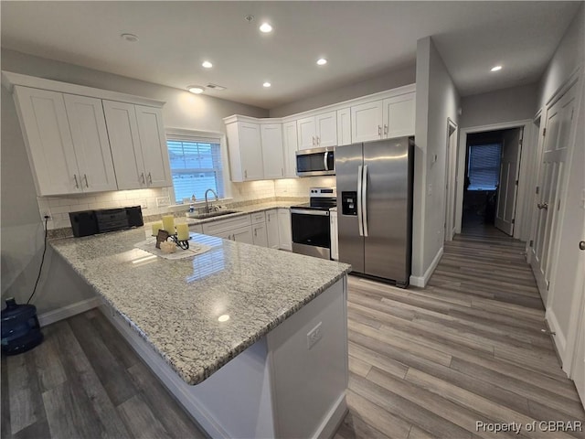 kitchen featuring white cabinetry, light stone countertops, kitchen peninsula, appliances with stainless steel finishes, and hardwood / wood-style flooring