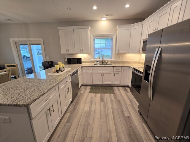 kitchen with white cabinets, sink, light wood-type flooring, appliances with stainless steel finishes, and light stone counters