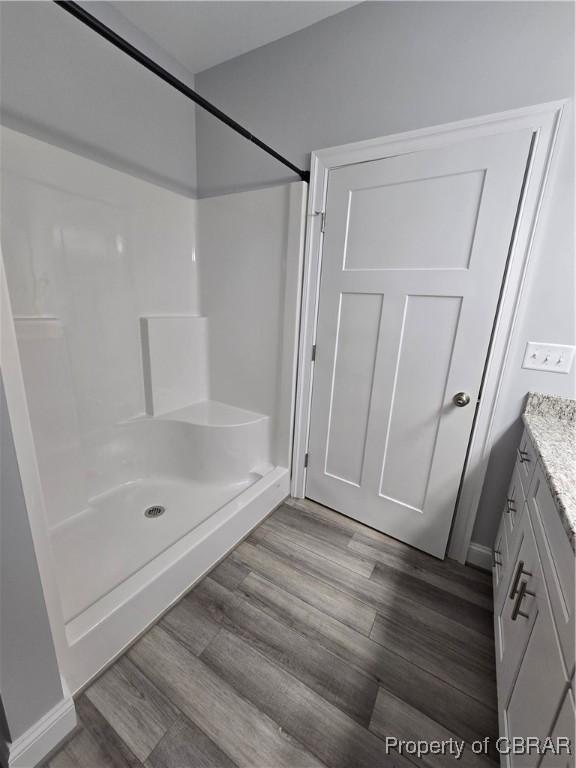 full bathroom featuring wood finished floors, a shower, and vanity