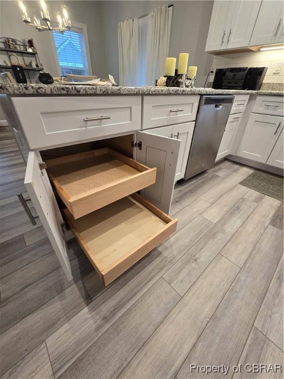 kitchen with light stone counters, an inviting chandelier, dishwasher, light hardwood / wood-style floors, and white cabinetry