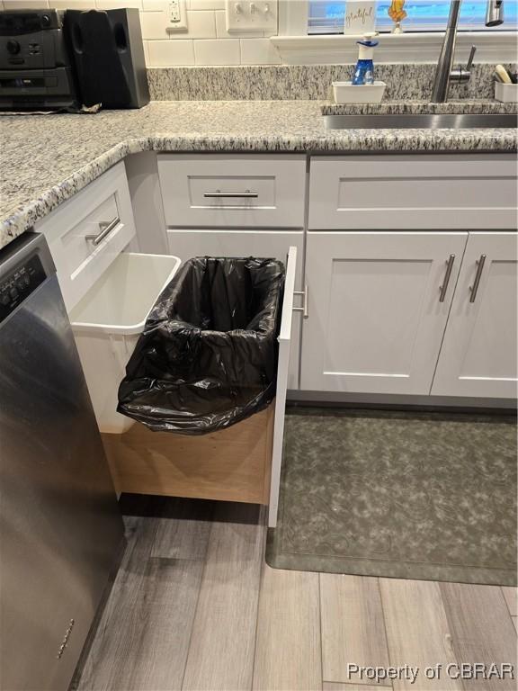 interior space with white cabinets, light stone counters, stainless steel dishwasher, and sink