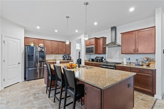 kitchen featuring a center island with sink, wall chimney range hood, sink, light stone countertops, and appliances with stainless steel finishes