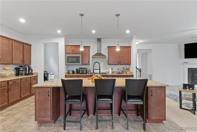 kitchen featuring decorative light fixtures, wall chimney range hood, and a kitchen island with sink