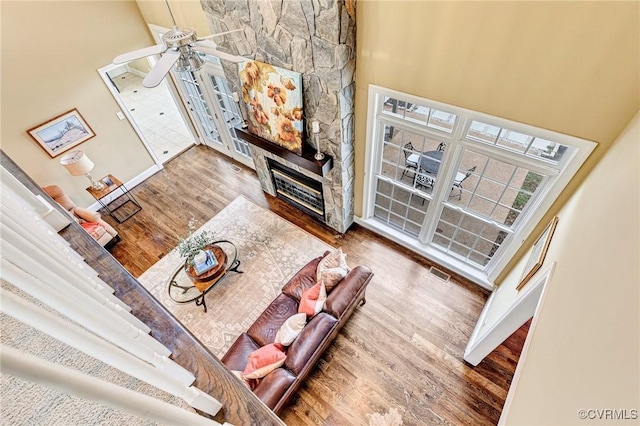 living room with hardwood / wood-style flooring, ceiling fan, a stone fireplace, and a towering ceiling