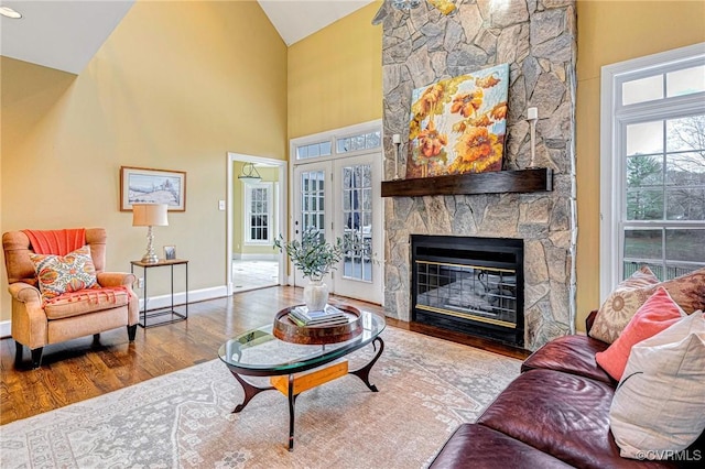 living room with hardwood / wood-style floors, high vaulted ceiling, and a stone fireplace