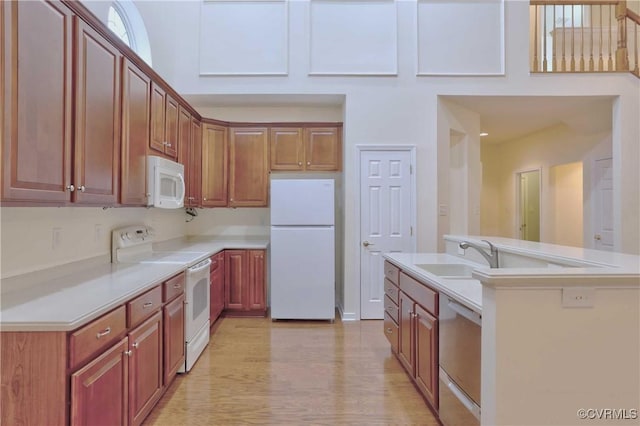 kitchen with white appliances, light hardwood / wood-style floors, a kitchen island with sink, and sink