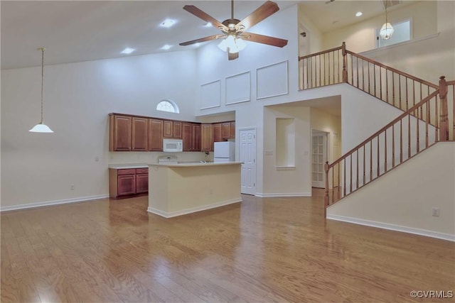 kitchen with white appliances, high vaulted ceiling, light hardwood / wood-style flooring, decorative light fixtures, and a kitchen island