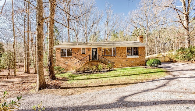 view of front facade with brick siding, crawl space, driveway, and a chimney