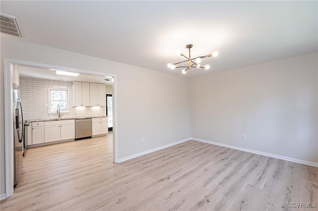 unfurnished dining area with light wood-type flooring, visible vents, a notable chandelier, a sink, and baseboards