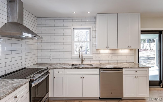 kitchen featuring light stone countertops, a sink, white cabinets, appliances with stainless steel finishes, and wall chimney exhaust hood