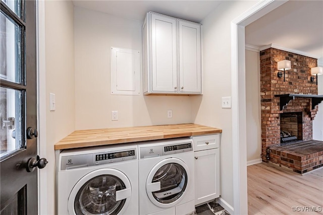 laundry area featuring light wood-type flooring, cabinet space, a fireplace, baseboards, and washing machine and clothes dryer