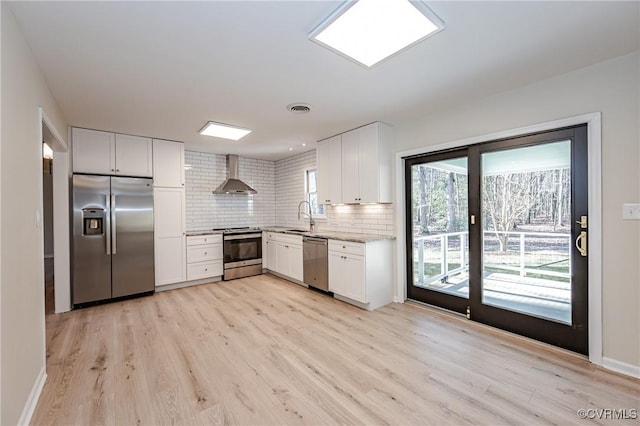 kitchen with visible vents, wall chimney range hood, decorative backsplash, appliances with stainless steel finishes, and a sink