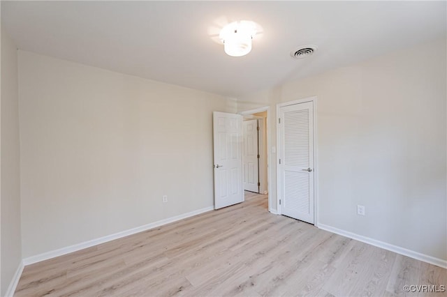 empty room with baseboards, visible vents, and light wood finished floors