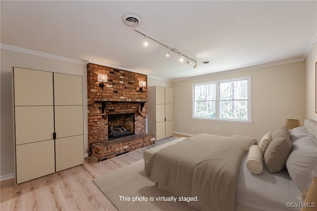 bedroom with visible vents, light wood finished floors, rail lighting, crown molding, and a brick fireplace