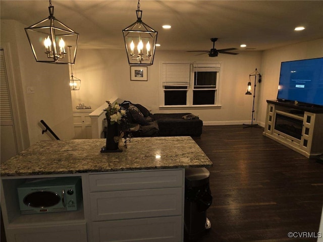 kitchen featuring dark hardwood / wood-style flooring, decorative light fixtures, a center island, and light stone countertops