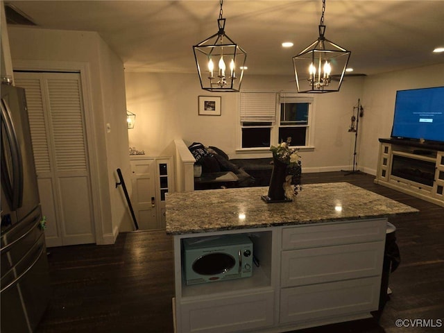 kitchen with decorative light fixtures, stainless steel fridge, light stone countertops, and a kitchen island