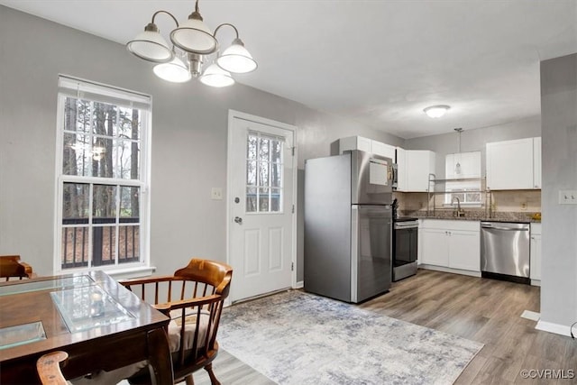 kitchen with hanging light fixtures, decorative backsplash, light hardwood / wood-style floors, white cabinetry, and stainless steel appliances