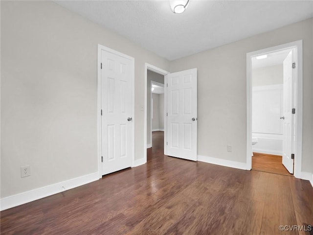 unfurnished bedroom with ensuite bath and dark hardwood / wood-style floors